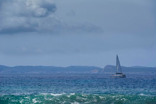 Small sailboat sailing in front of an island. Sky with clouds. Mediterranean sea. Balearic Islands. Empty space