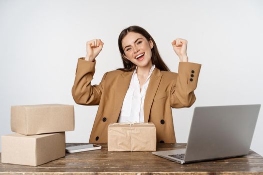 Happy smiling female entrepreneur, small business owner working with client orders on website, packing boxes for delivery, standing over white background.