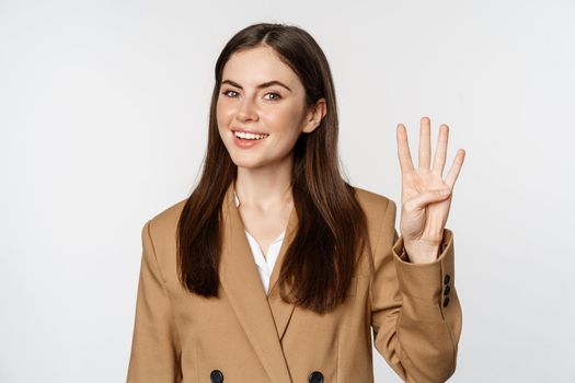 Portrait of corporate woman, saleswoman showing number four fingers and smiling, standing in suit over white background.