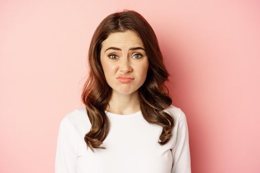 Close up portrait, face of woman cringe, grimacing disappointed, looking awkward or upset, standing over pink background.