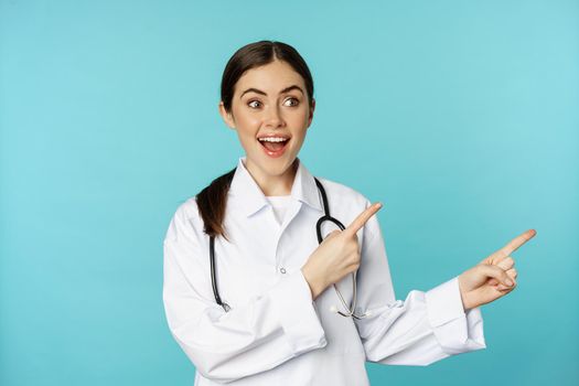 Portrait of young professional doctor, woman hospital worker, pointing fingers right, showing logo, clinic promo deal, standing over torquoise background.