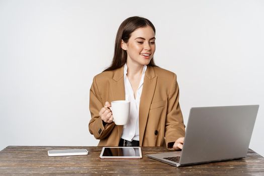 Portrait of office woman, ceo entrepreneur working on laptop, drinking coffee and answer clients on website, standing over white background.