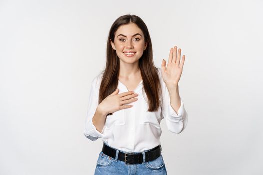 Friendly cute woman raising hand and introduce herself, saying name, pointing at her, saying hello, standing over white background.