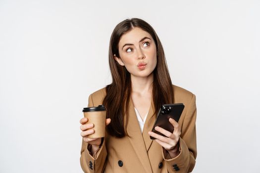 Portrait of saleswoman, corporate woman drinking takeaway coffee and reading smartphone, looking at mobile phone, white background.