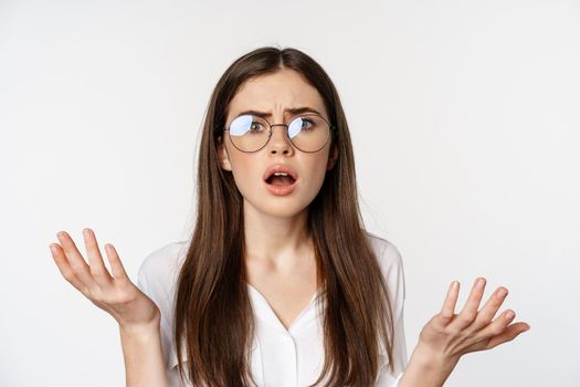 Close up of confused brunette woman in glasses, looking puzzled and clueless, standing over white background. Copy space