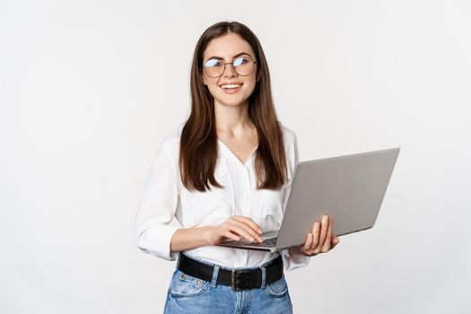 Portrait of young office woman, entrepreneur answer clients on laptop, working with computer with happy face, standing over white background.