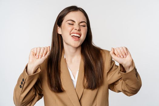 Successful businesswoman, saleswoman dancing and having fun, wearing office suit, posing over white background.