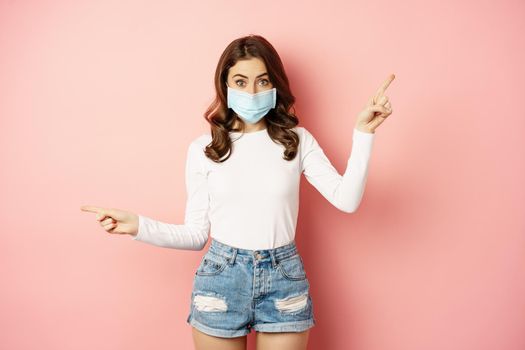 Portrait of beautiful woman in face medical mask pointing sideways, showing two choices, ways, sides, demonstrating advertisement, pink background.