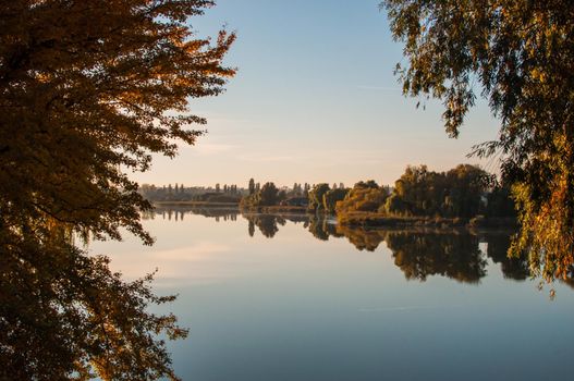 sunset against the background of the river in September in the harvest season. Reflection in the water from the trees. Beautiful autumn landscape. Autumn colors are reflected in calm waters.