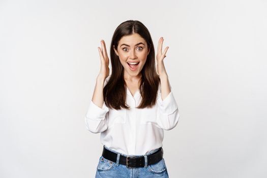 Excited young adult woman reacting to win, surprise news, screaming and cheering, triumphing, achieve goal and celebrating, standing over white background.