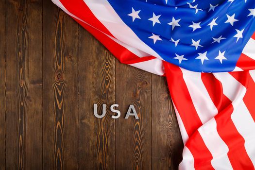 the word USA laid with silver metal letters on wooden board surface with crumpled flag of United States of America in upper right side, directly above perspective