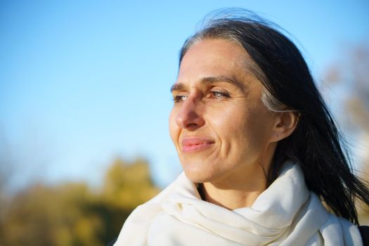 Profile side view portrait of attractive cheerful dreamy grey-haired middle-aged woman relaxing outdoors during sunny day.