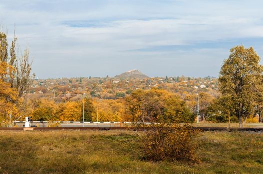 Autumn sunny landscape. View of a mining autumn city with trees and fallen yellow leaves on the ground on a sunny October day. Template for design.