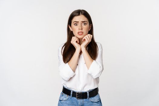 Portrait of brunette woman looking concerned, worried and shocked, standing overwhelmed against white background.