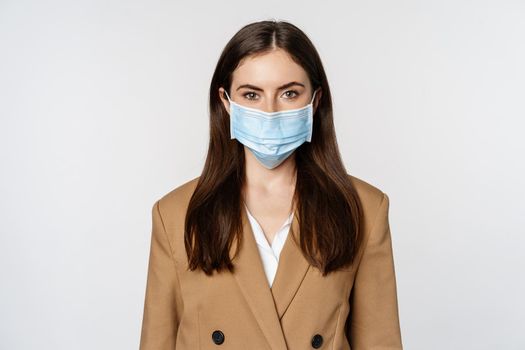 Workaplce and pandemic concept. Face portrait of businesswoman in medical mask and suit, looking serious at camera, going to work during covid-19.