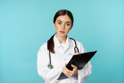 Image of professional woman doctor, physician with clipboard writing, listening patient at hospital clinic appointment, standing over torquoise background.