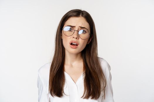 Close up of confused brunette woman in glasses, looking puzzled and clueless, standing over white background. Copy space