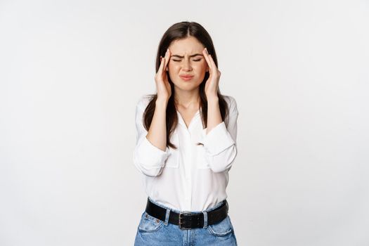 Corporate woman grimacing, touching head, feeling headache, severe migraine, standing over white background.