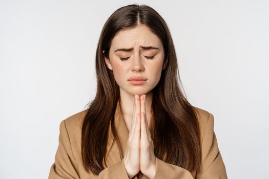 Sad hopeful businesswoman praying, close eyes and supplicating, close eyes and pleading, standing over white background.