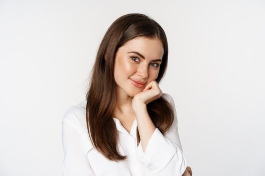 Close up of beautiful, coquettish brunette woman, blushing and smiling flirty, posing against white background. Copy space