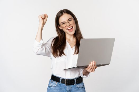 Enthusiastic office woman, businesswoman holding laptop and shouting with joy, celebrating and rejoicing, standing over white background.