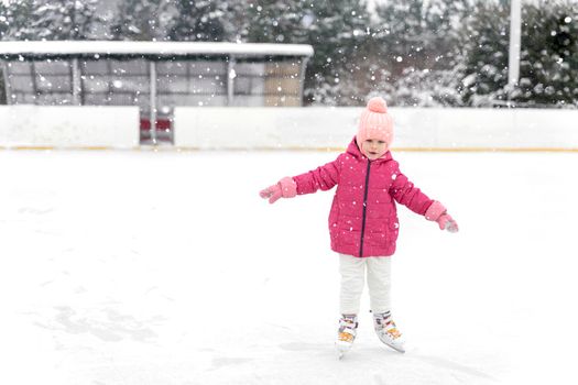 child girl in a red jacket skates on a skating rink in heavy snow