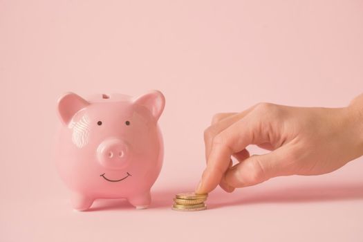A woman's hand puts coins next to a piggy bank close-up, a girl saves her salary, plans savings, invests in her future.