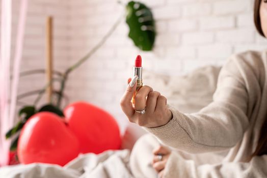 Valentine's day, Women's day. Brunette young caucasian Woman sitting on the bed making up coloring lips