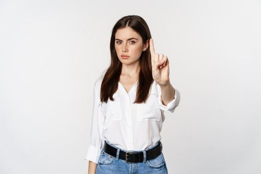 Serious woman showing taboo, stop gesture, shaking finger in disapproval, disagree, forbidding something, standing over white background.