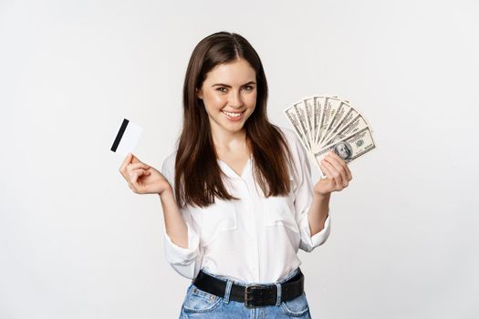 Happy woman holding money and credit card with thoughtful face, concept of loan and microcredit, standing over white background.