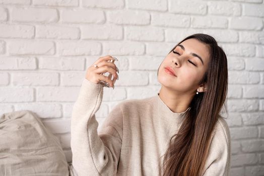 Valentine's day, Women's day. Brunette young caucasian Woman sitting on the bed making up applying perfume