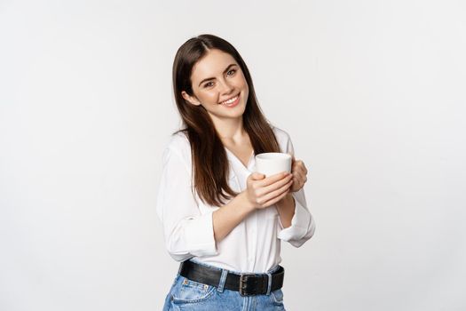 Corporate woman standing with coffee tea mug and smiling, drinking from cup, standing happy against white background.