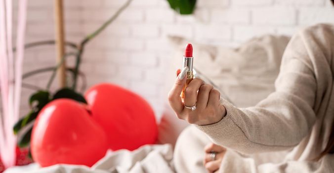 Valentine's day, Women's day. Brunette young caucasian Woman sitting on the bed making up coloring lips