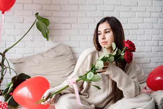 Valentine's day, Women's day. Young caucasian brunette woman sitting in the bed celebrating valentine day smelling red roses