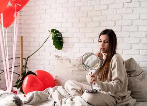 Valentine's day, Women's day. Brunette young caucasian Woman sitting on the bed making up coloring lips