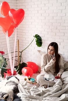 Valentine's day, Women's day. Brunette young Woman celebrating valentines day, sitting on the bed making up