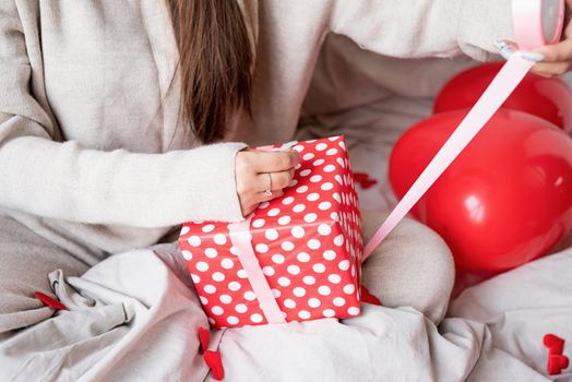 Valentine's day, Women's day. Young caucasian brunette woman sitting in the bed celebrating valentine day wrapping the gifts