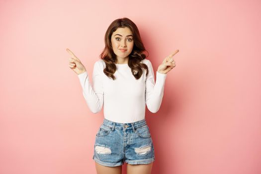 Glamour indecisive girlfriend, shrugging and pointing fingers sideways, showing left and right promo text, store offers, confused what to choose, pink background.