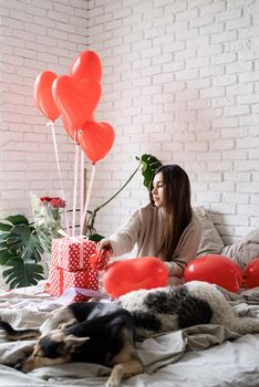 Valentine's day, Women's day. Young caucasian brunette woman sitting in the bed celebrating valentine day wrapping the gifts