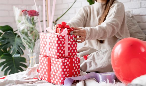 Valentine's day, Women's day. Young caucasian brunette woman sitting in the bed celebrating valentine day wrapping the gifts