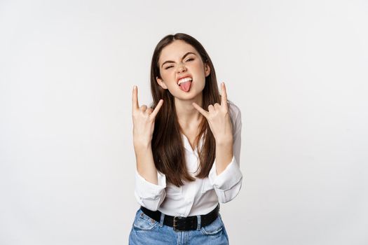 Rock n roll. Young woman showing rock on, heavy metal sign, having fun, standing carefree against white background.