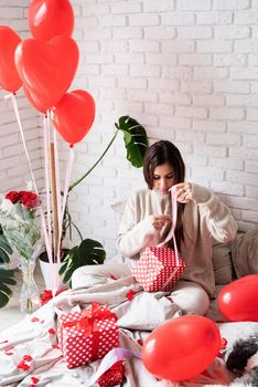 Valentine's day, Women's day. Young caucasian brunette woman sitting in the bed celebrating valentine day wrapping the gifts