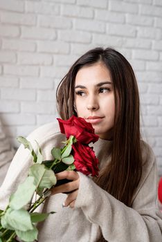 Valentine's day, Women's day. Young caucasian brunette woman sitting in the bed celebrating valentine day smelling red roses