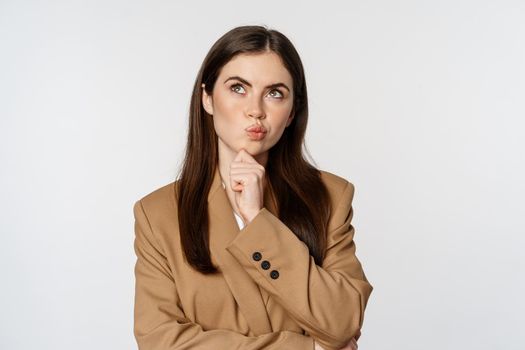 Image of businesswoman thinking, corporate woman looking thoughtful, making decision, standing in brown suit over white background.