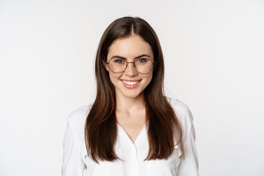 Close up portrait of smiling girl entrepreneur, office woman in glasses, looking happy and confident, standing in white blouse over studio background.