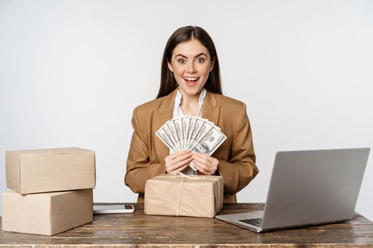 Portrait of businesswoman sitting in office with money, working and making profit income, posing happy against white studio background.