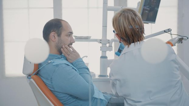 Dentist and patient talking about teeth radiography scan at stomatological examination in cabinet. Expert explaining x ray diagnosis to adult in pain, using dentistry equipment.