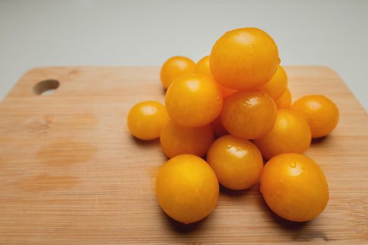 Close-up of yellow cherry tomatoes lie in a pyramid on a wooden cutting board. Vegetarian food.