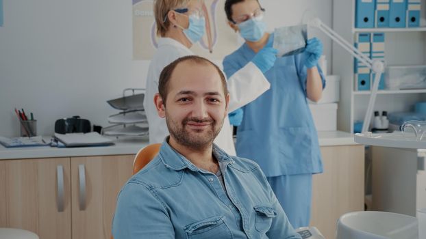 Portrait of oral care patient smiling and looking at camera, sitting in dentistry cabinet. Man having checkup appointment with stomatologist to treat caries problems at dental clinic.