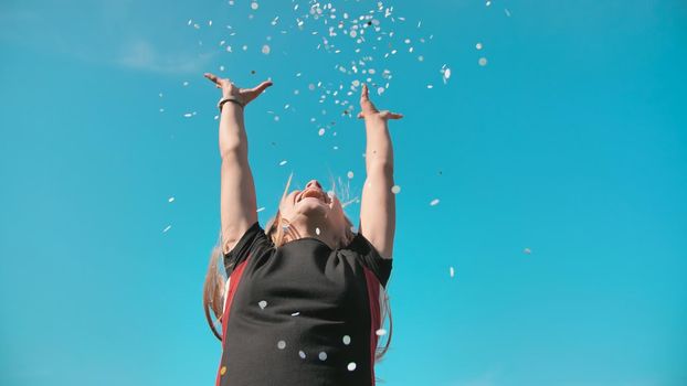 Success concept. Teen girl throws a multi-colored confetti into the blue sky